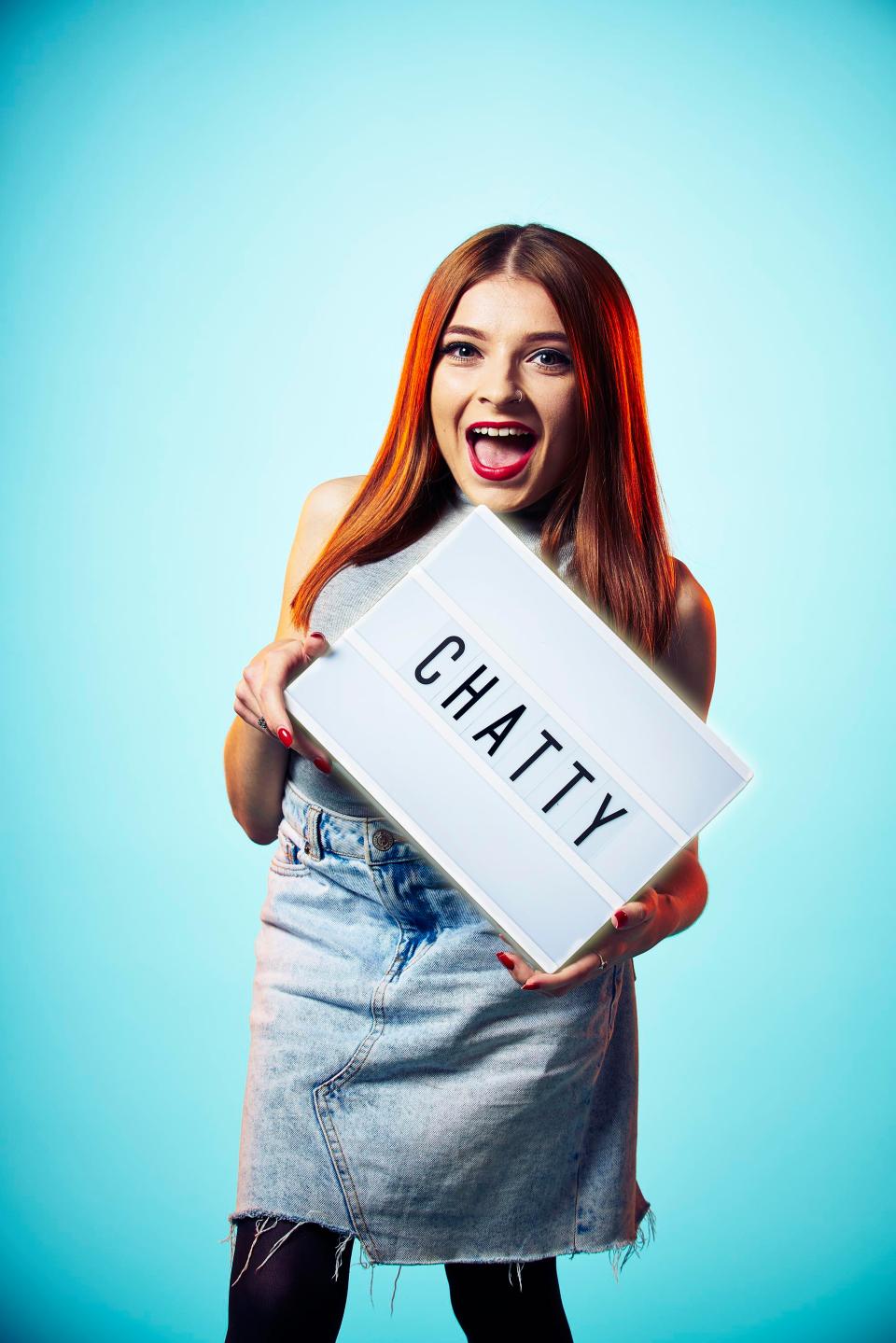 Becky Dann of The Undateables stands holiding a sign with the word 'Chatty'