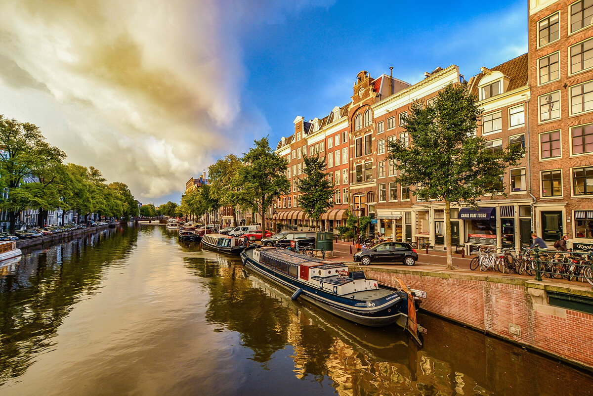 5 of the Safest Cities to Navigate With a Disability: Boats lined up along a canal in Amsterdam during a beautiful sunny.