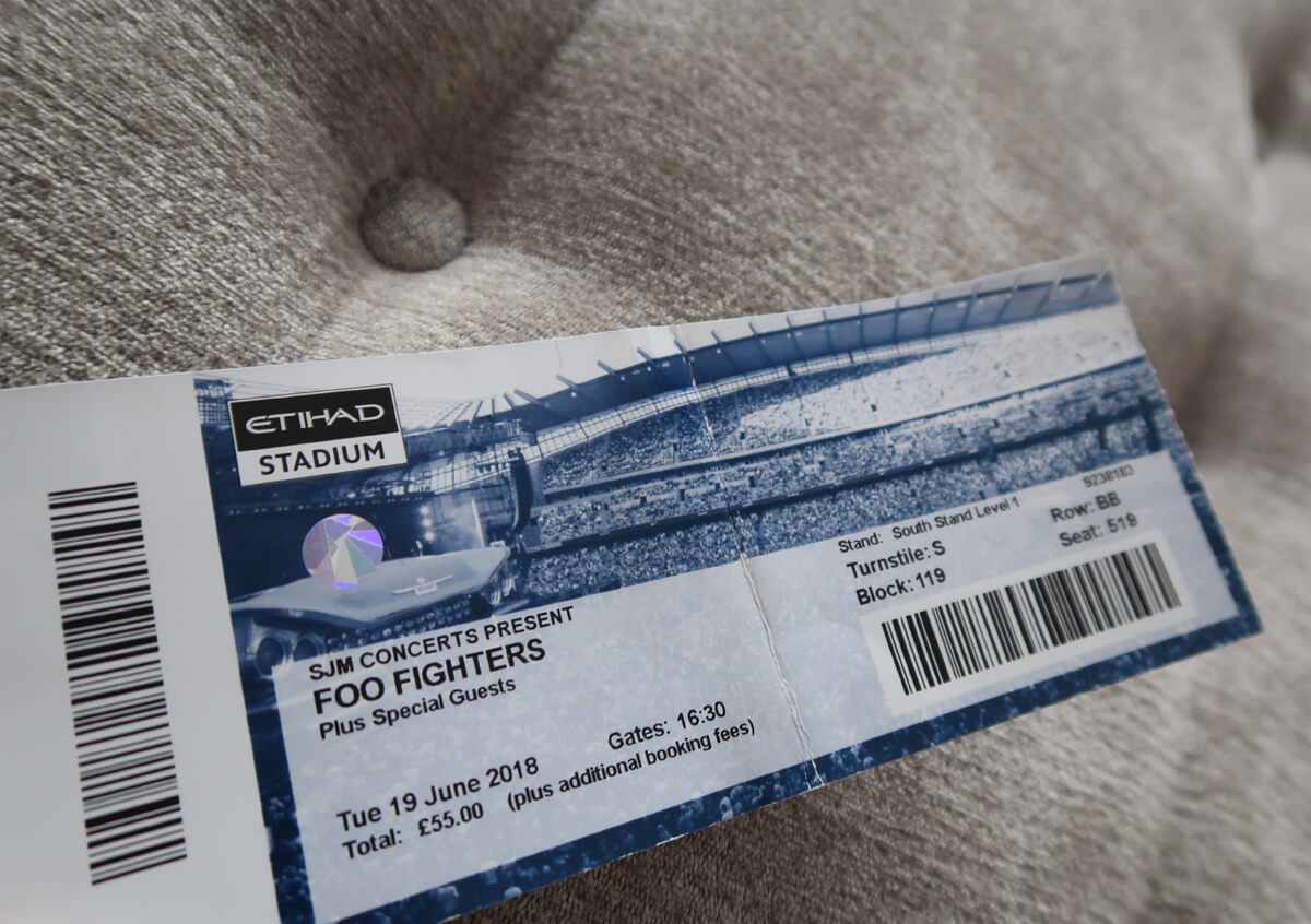 A Foo Fighters gig ticket for Manchester Etihad Stadium laying on a grey material background.