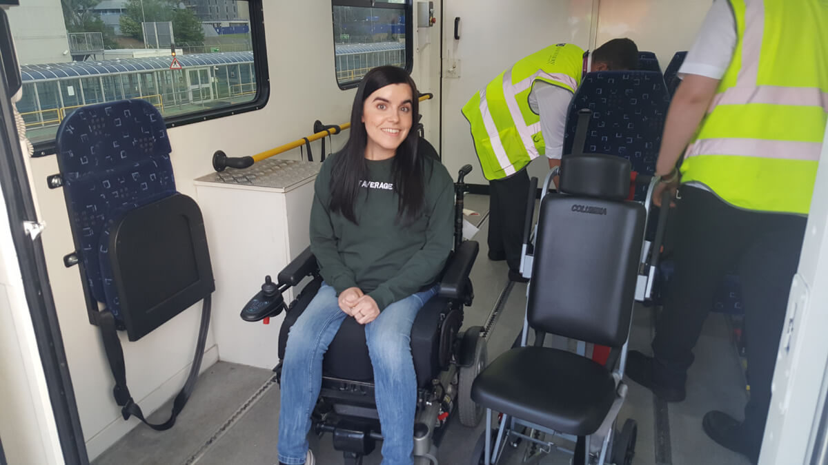 Emma sitting in her power wheelchair waiting to be transferred into an aisle chair by two special assistance agents.