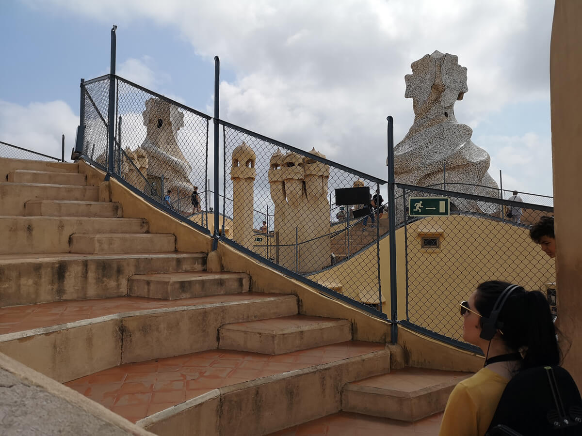 Emma is sitting on the roof of Casa Milà. She is unable to move around due to lack of wheelchair access. Emma is looking at the steps wearing the audio headset.