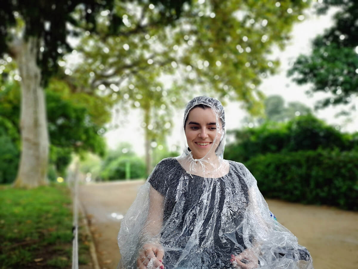 Emma is wearing a poncho while sheltering under trees in Parc de la Ciutadella during a thunderstorm.