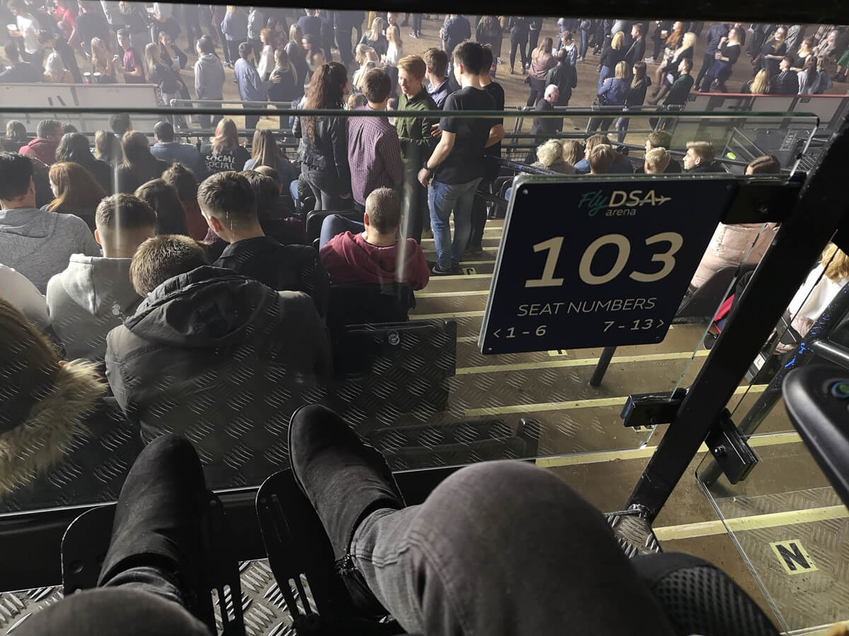A view looking down Emma's legs and and feet on her wheelchair footplates. Emma is sitting in section 103 accessible seating bays at FlyDSA Arena Sheffield.