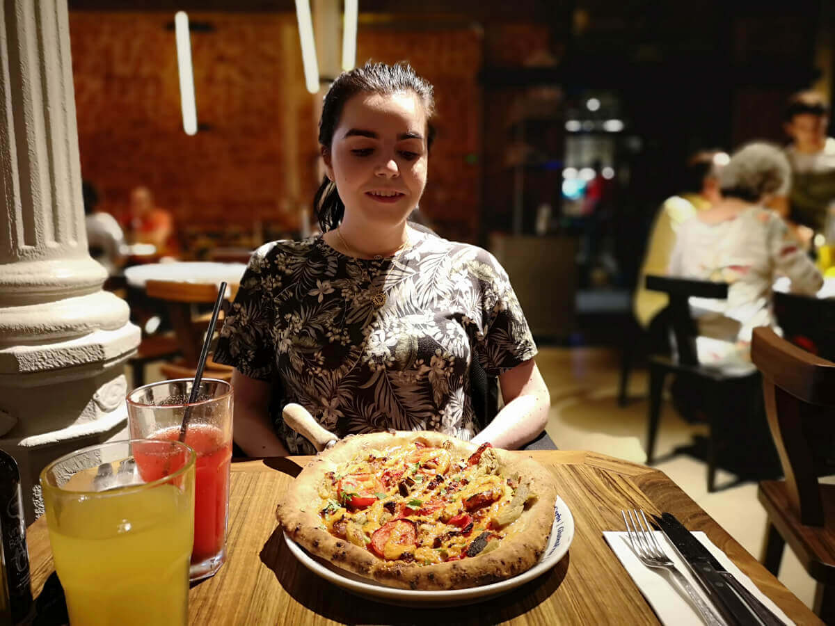 Emma looking down at her vegan pizza in Flax & Kale Passage.