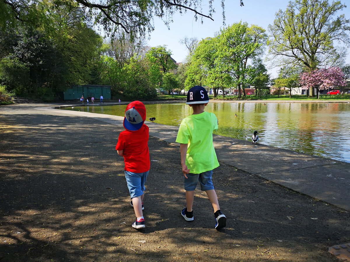 Emma's two nephews walking alongside pond in the park during a sunny day.