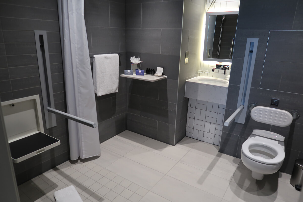 Accessible bathroom with grey slate wall tiles. The bathroom is large with toilet, wash basin, sink and roll-in shower.