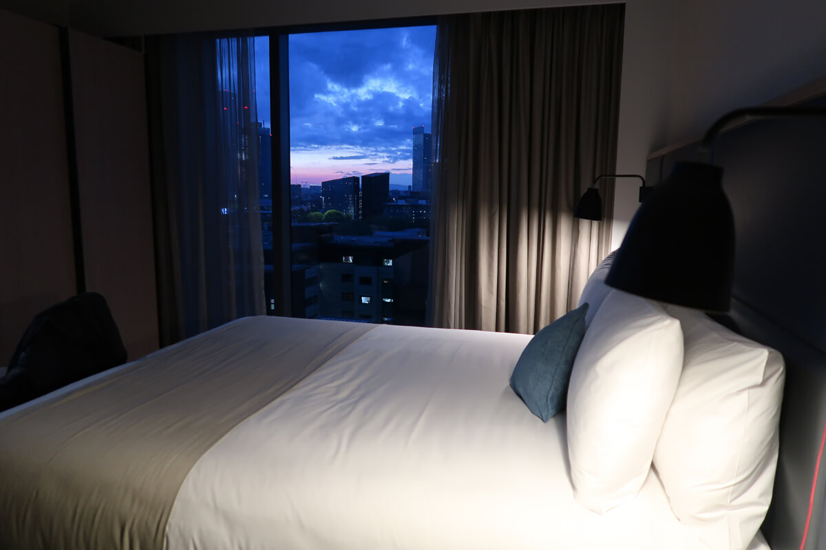 View of the sunset sky from our hotel room. The large queen sized bed is in the shot as well with the blue, purple and pink sky in the background.