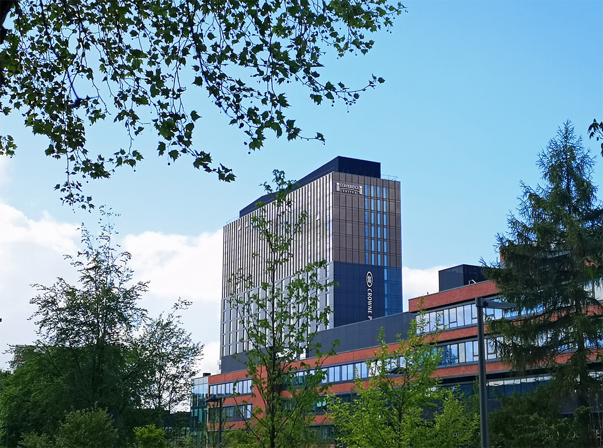 An exterior shot of Crowne Plaza Manchester from a distance. There are trees framing the photo.