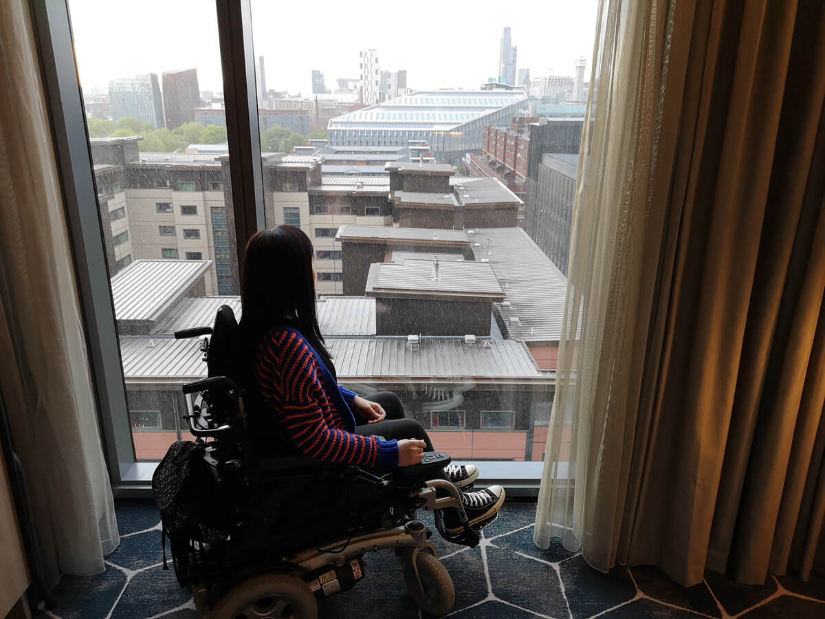 Emma sitting at the large hotel room window. She is looking out and enjoying the view.