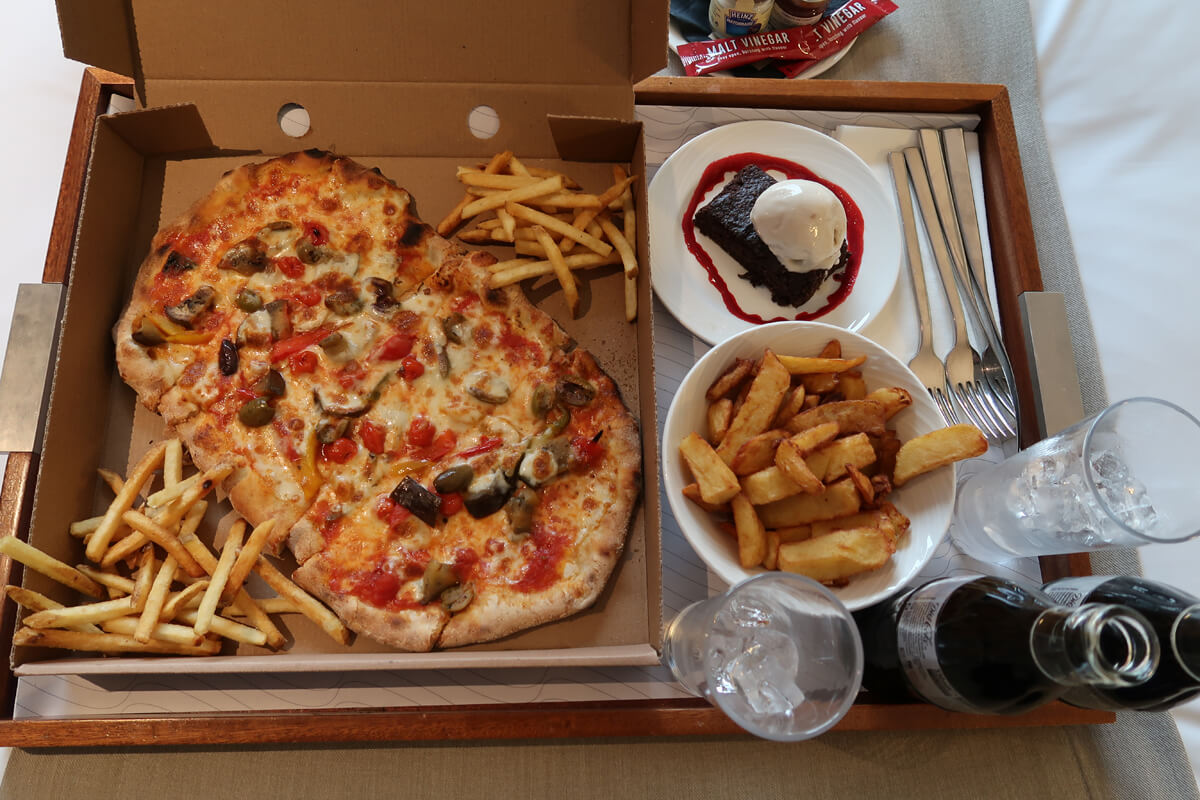A vegan pizza with fries, a vegan chocolate brownie on a room service tray.
