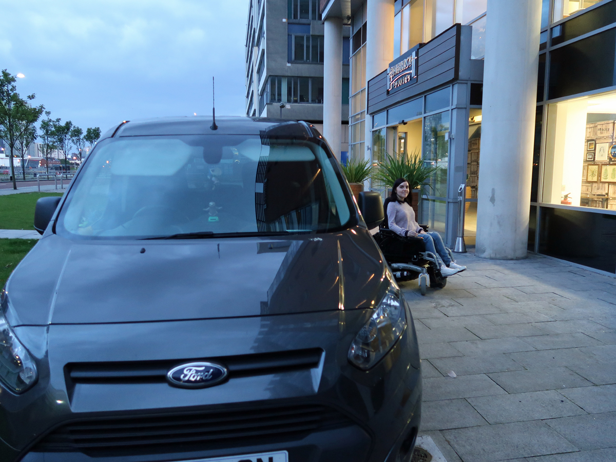 Emma sitting in her wheelchair beside her car outside the hotel in Liverpool.