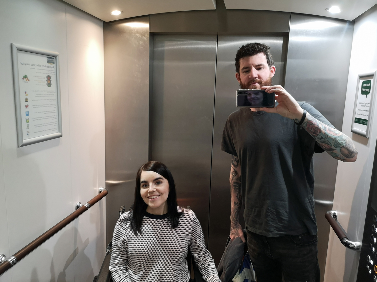 Emma and Allan inside the lift taking a selfie in the lift mirror.