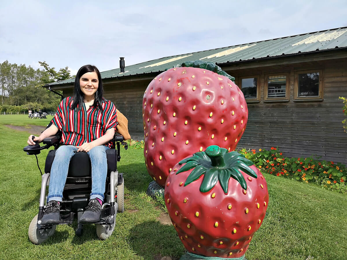 Emma sitting in her wheelchair next to two giant strawberry statues.