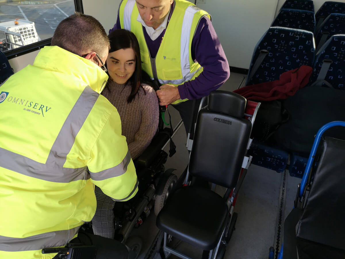 Emma being lifted out of her wheelchair by two special assistance workers.