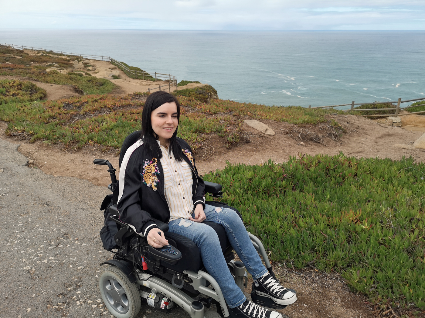 Emma in her wheelchair sitting with the ocean behind her in Portugal.