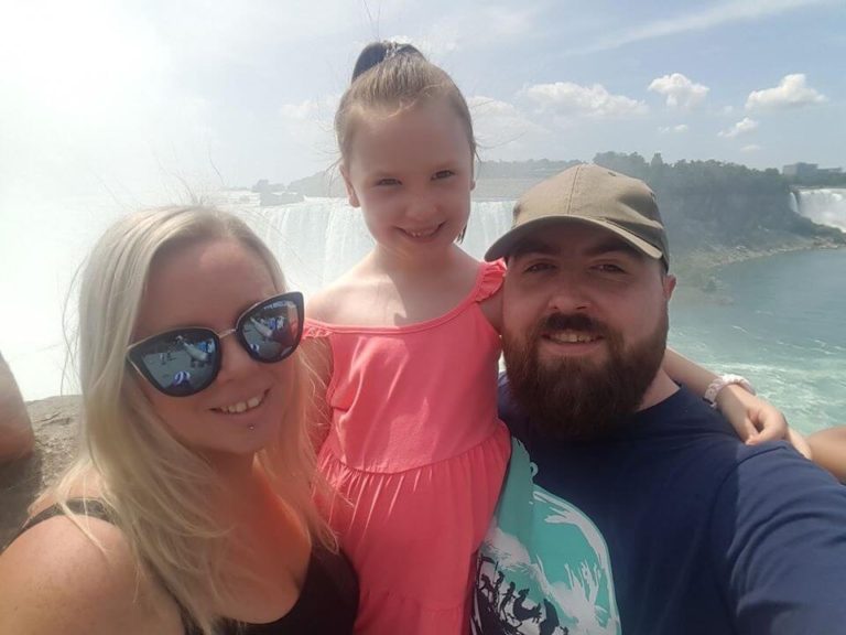 Joe, his wife and daughter smiling at the camera with the Niagara Falls behind them.