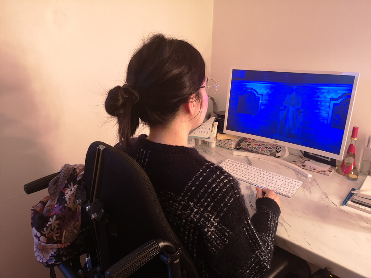 Emma sitting in her wheelchair with her back facing the camera. She is at her desktop PC watching Dermot Kennedy's virtual gig.