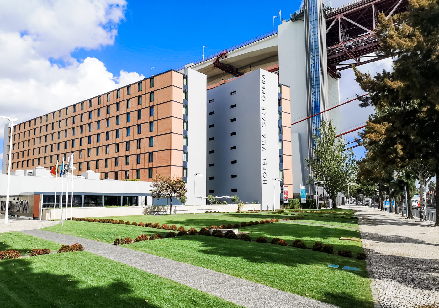 An exterior view of Vila Galé Ópera hotel with the 25th April Bridge running across overhead.