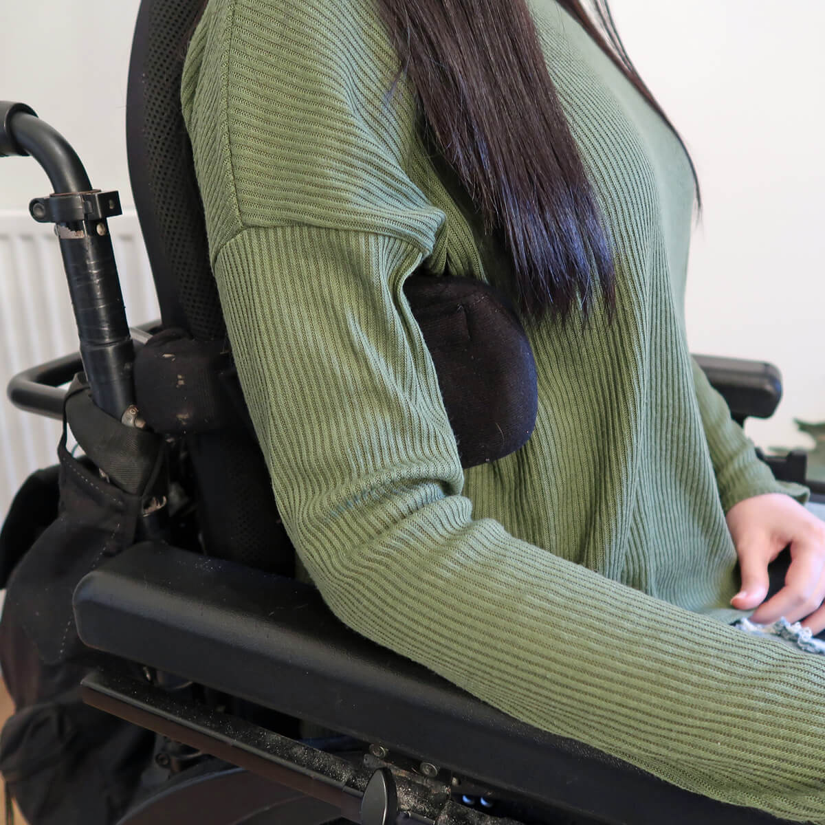 A close up of Emma's torso while sitting in her wheelchair. She has a side lateral support attached to her wheelchair. It is tucked under her arm supporting her in an upright position. 