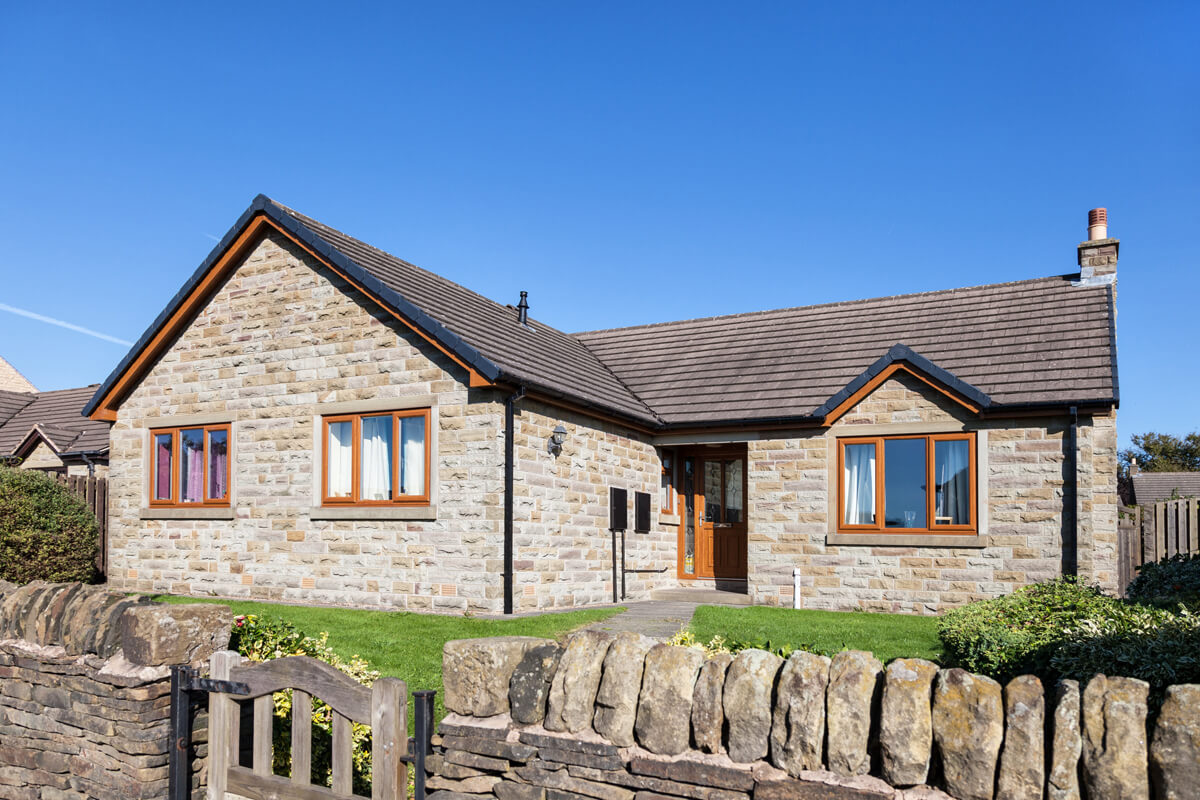traditional stone bungalow with brown wooden windows and drystone wall at the front