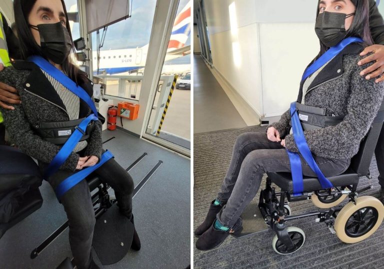 Emma strapped into an aisle chair at London City Airport. The heel of Emma's boots are on the footplate while her feet are pointing directly down to the ground. Emma is looking at the camera with a worried look on her face. The special assistance agent has his hand on Emma's shoulder so she doesn't fall over due to the lack of postural support on the aisle chair.
