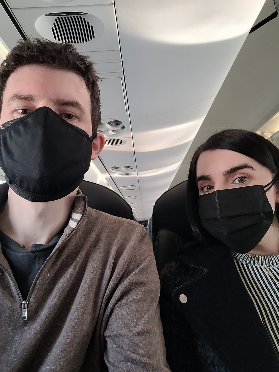 A selfie of Allan and Emma sitting on a plane. They are wearing black face masks.