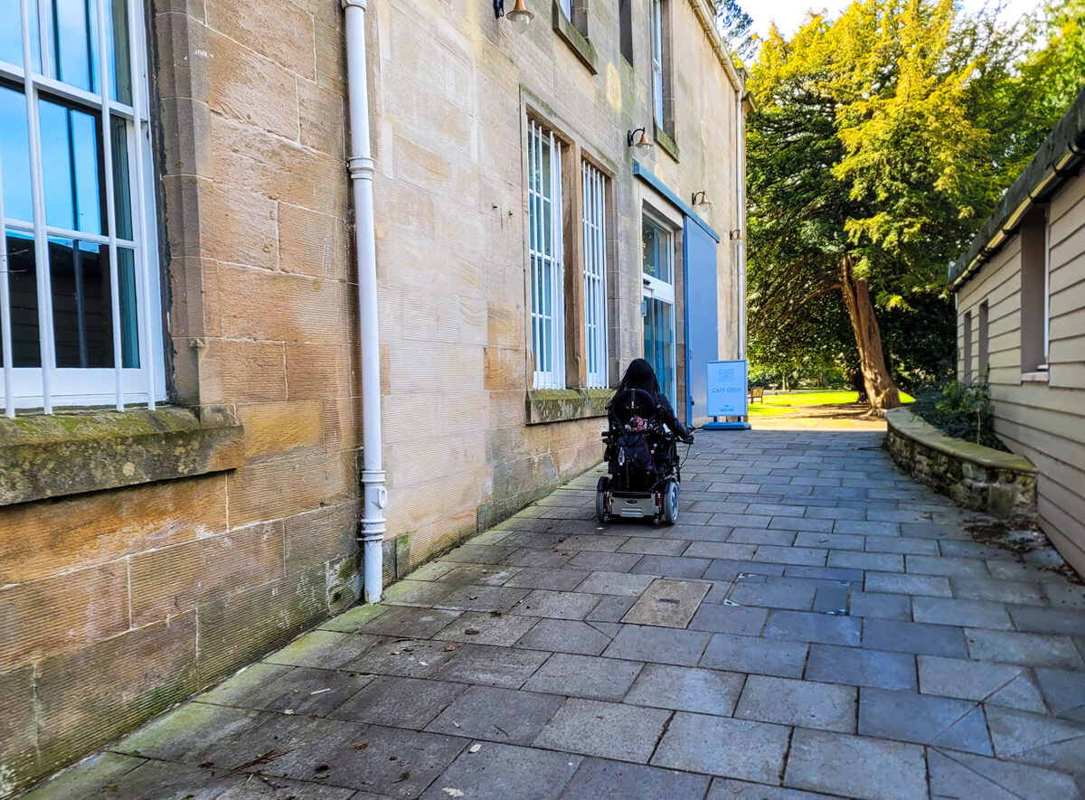 Emma pictured from the back driving up a sloped path into Arnotdale House & Cafe at Dollar Park in Falkirk