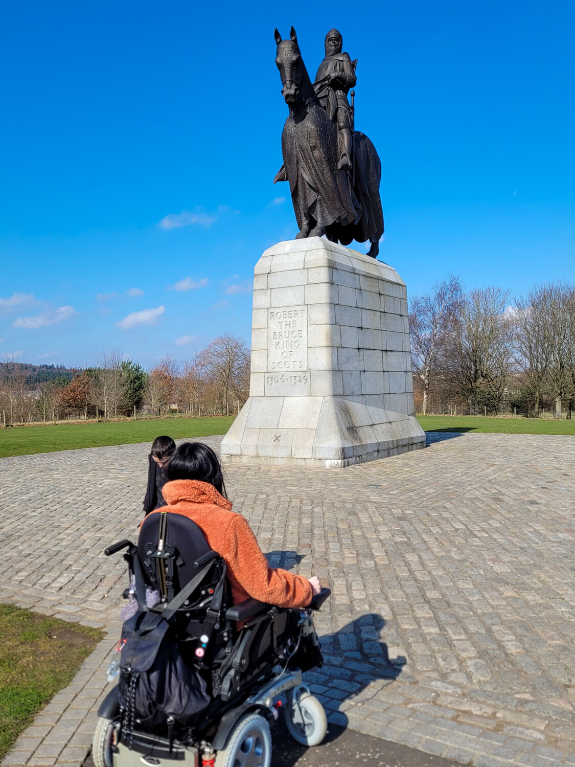 Emma sat in her wheelchair photographed from the back. She is facing towards the statue of King Robert Bruce.