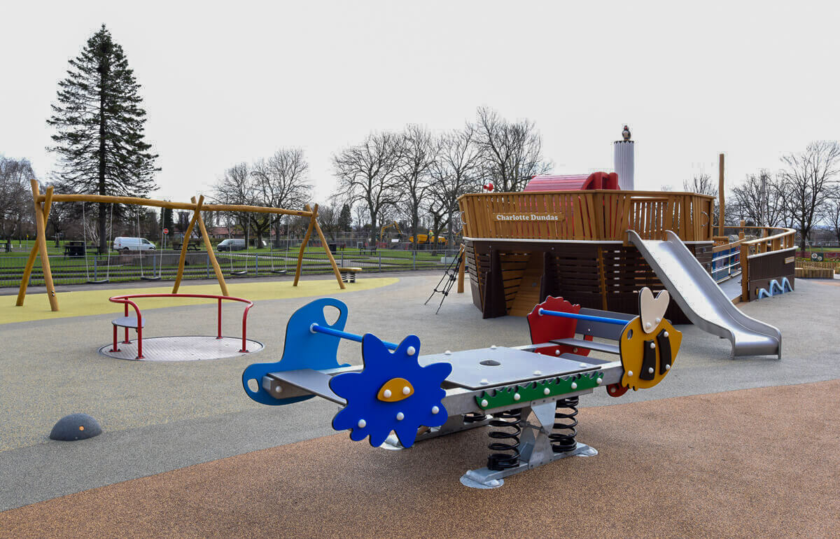 Kids play area with inclusive play equipment including wheelchair accessible roundabout.
