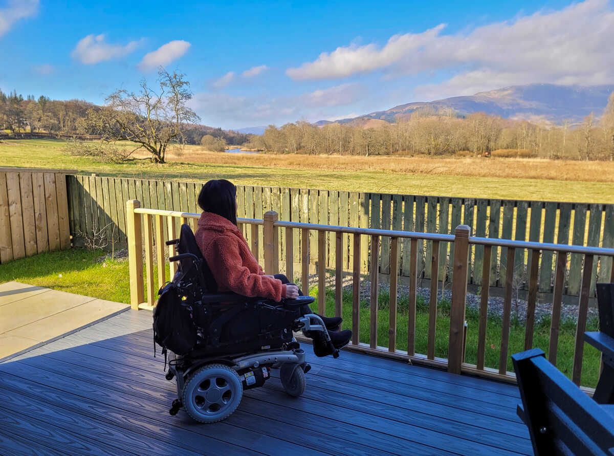 Emma sat in her powered wheelchair outside on the pod decking looking across the fields to the mountains.