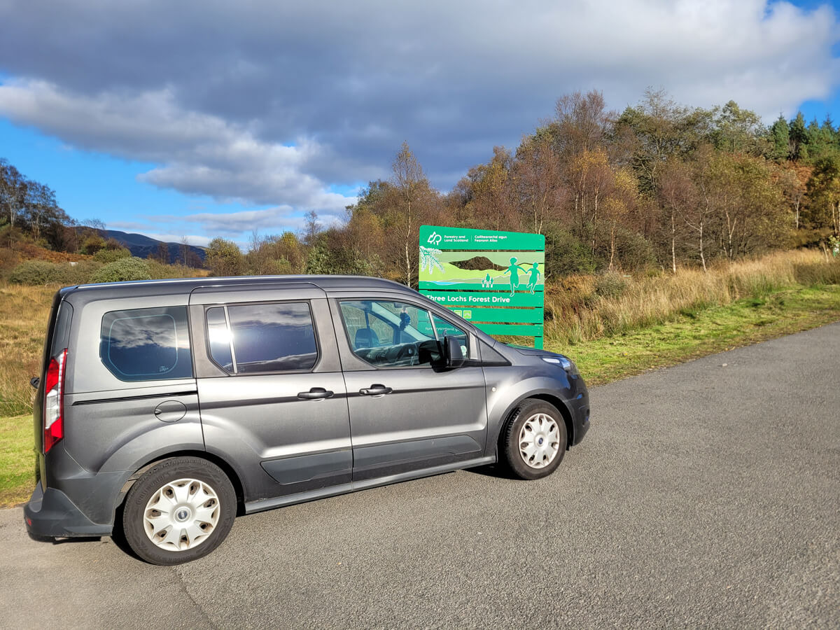 Emma's grey WAV parked on the road at the entrance of the Three Lochs Forest Drive 