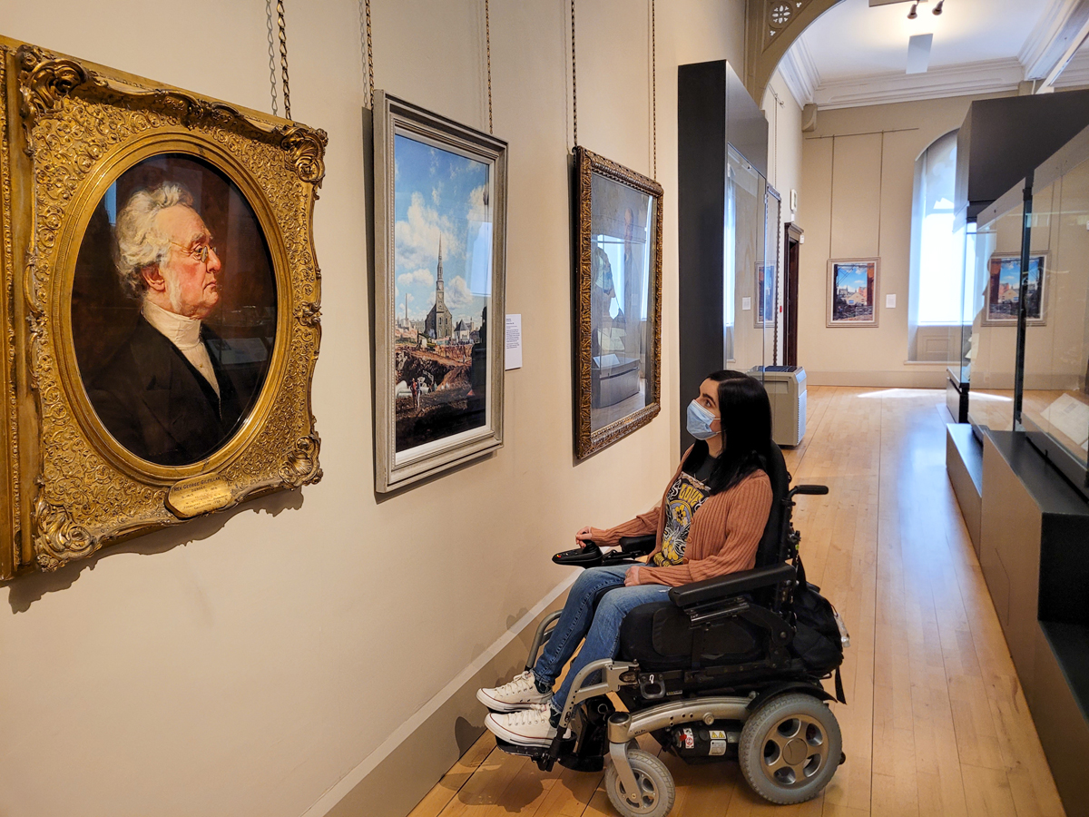 Emma sat in her powered wheelchair looking at paintings hung on the wall at the McManus Museum.