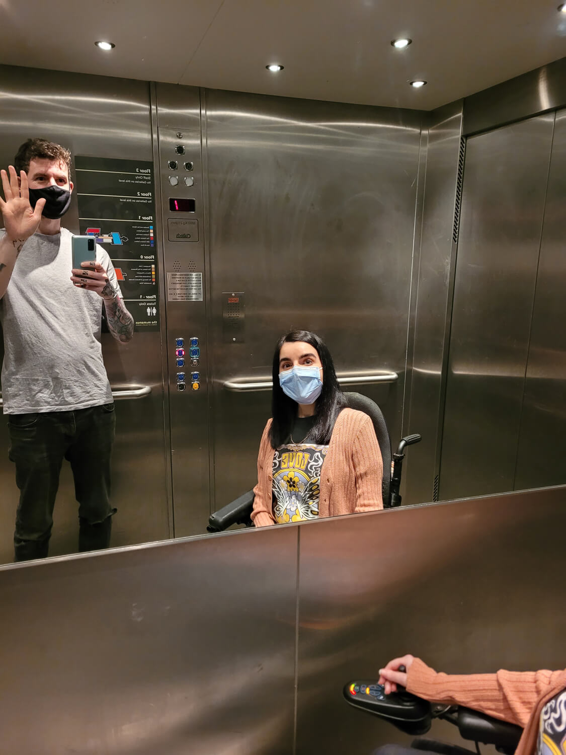 Emma and Allan taking a mirror selfie inside the lift. They are both wearing face masks.
