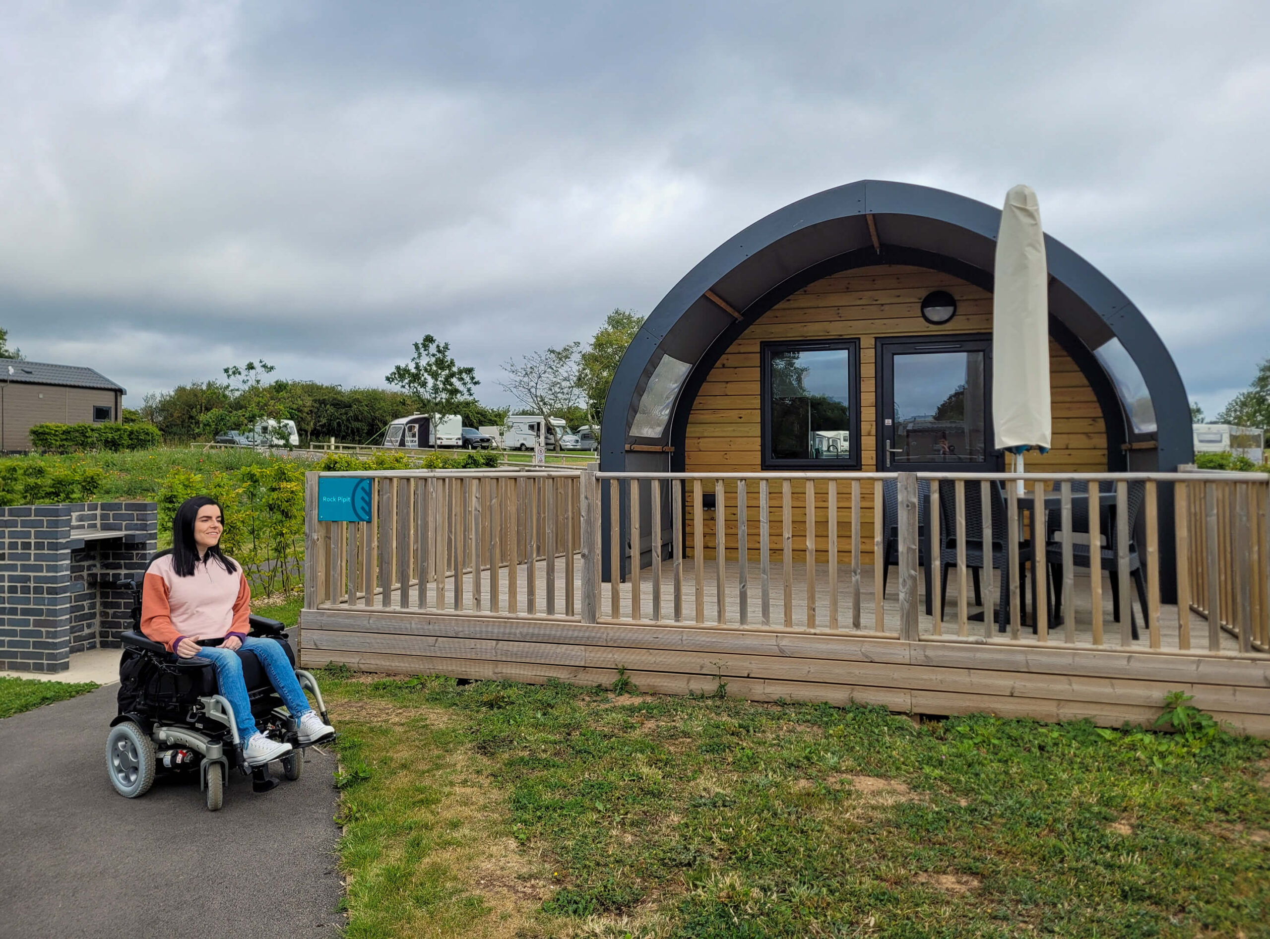 Emma sat in her wheelchair outside next to the wheelchair accessible glamping pod at Cayton Village.
