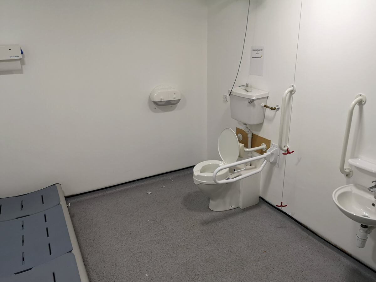 Interior of a Changing Places toilet showing the adult-sized changing bed and peninsular toilet.