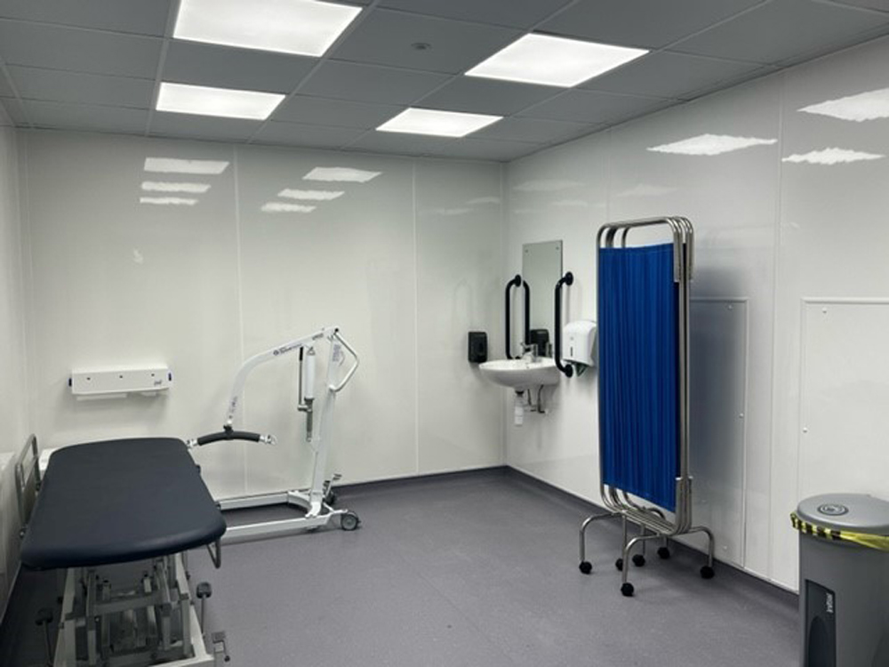 Interior of a Changing Places toilet showing the adult-sized changing bed, peninsular toilet and sink, mobile hoist, grab rails.