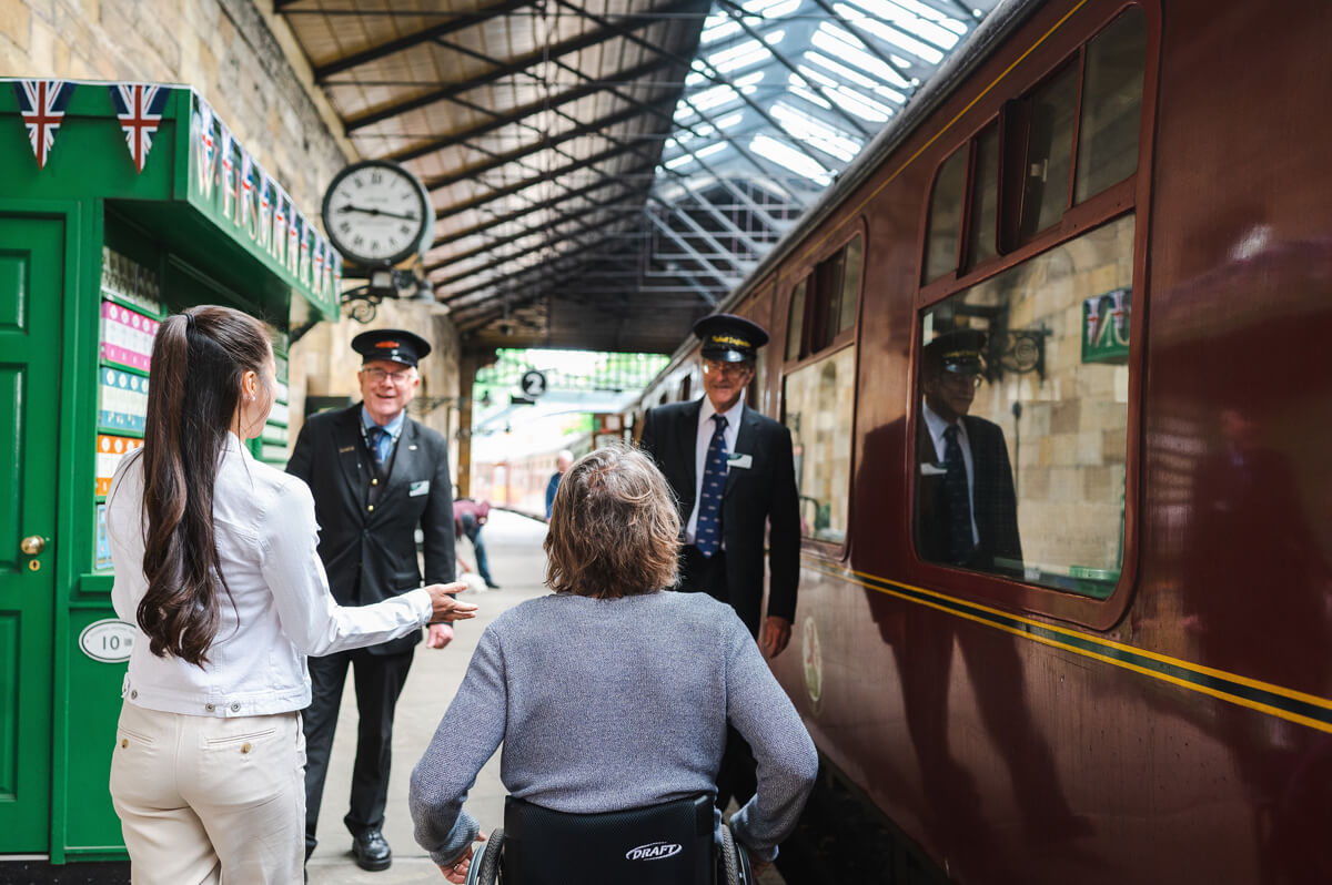Man in a wheelchair and woman talking to the railway staff a steam engine.