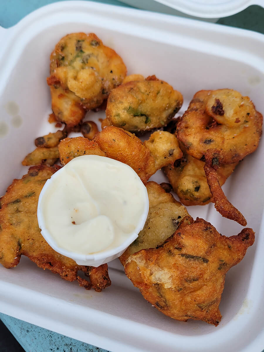 Bean and lentil fritters and a mayo dip in a white takeaway box.