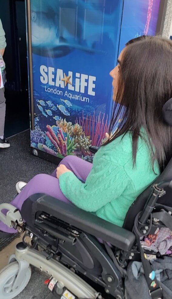 Emma sat in her wheelchair driving through the main entrance to SEA LIFE London Aquarium