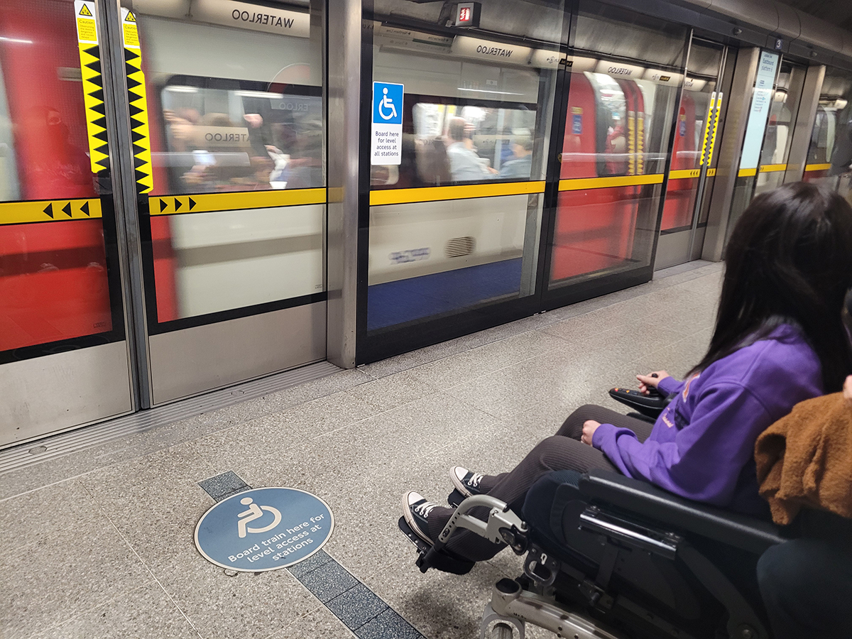 Emma sat in her wheelchair at the wheelchair boarding spot on the platform waiting on the tube.