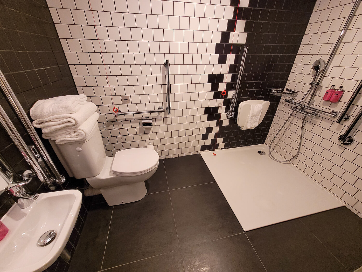 An accessible bathroom with a roll-in shower and wall mounted shower seat at the Moxy Manchester City hotel.