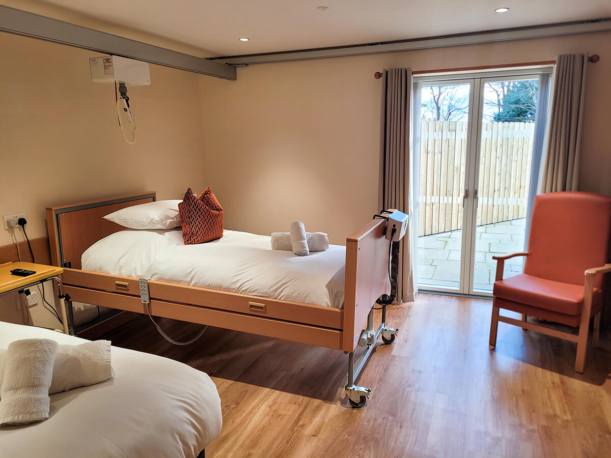 The accessible twin room with a height adjustable profiling bed with an Invacare pressure relief air mattress. Ceiling track hoist above the bed.