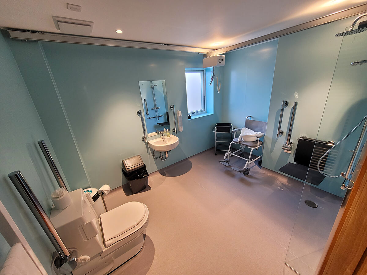 A large wet room in the Durham accessible lodge at Homelands. It has a clos-o-mat toilet, shower with wall mounted seat, shower commode chair.