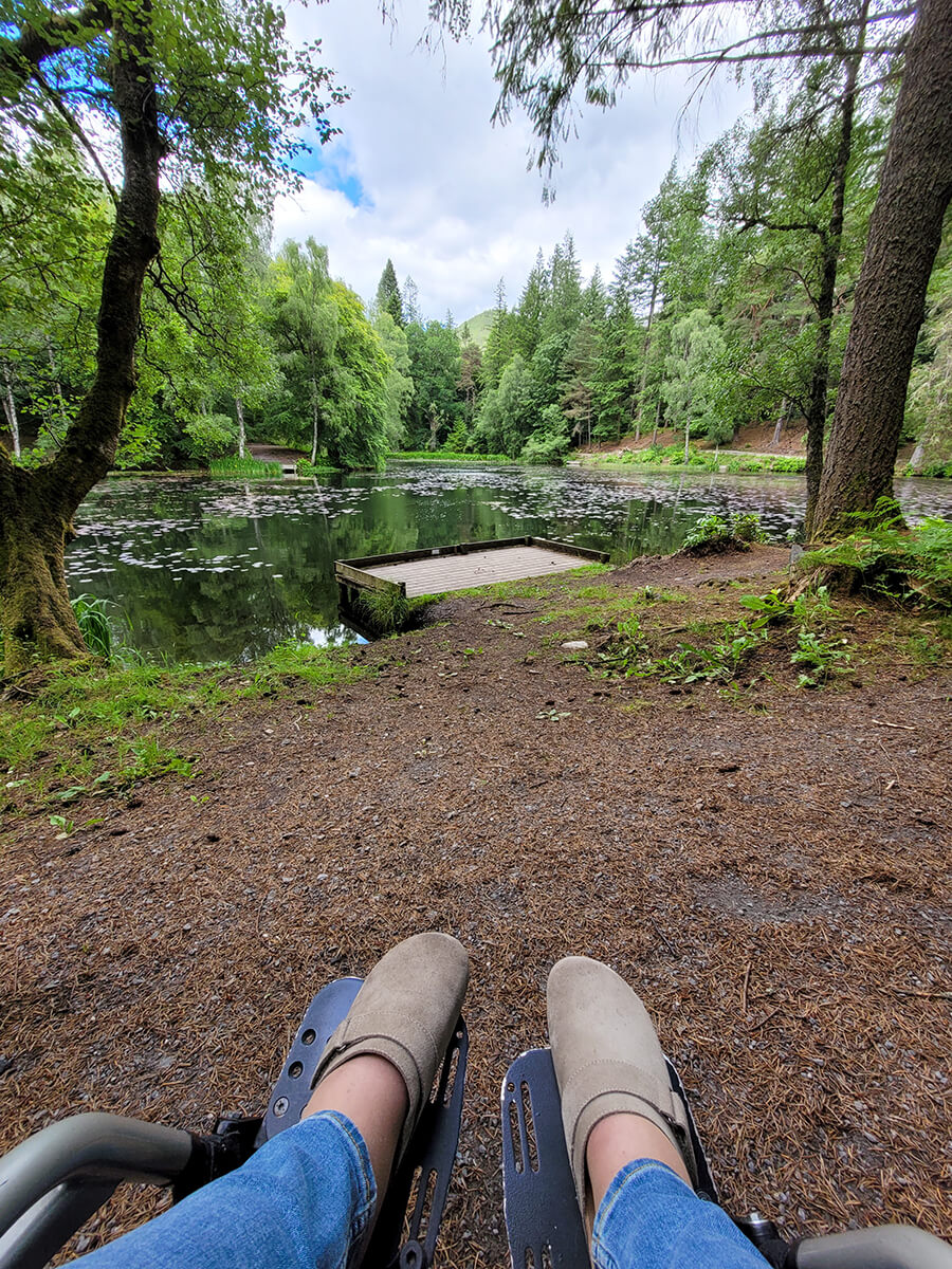 A shot looking down at Emma's legs on her wheelchair footplates and a view of Loch Dunmore in Faskally Woods.