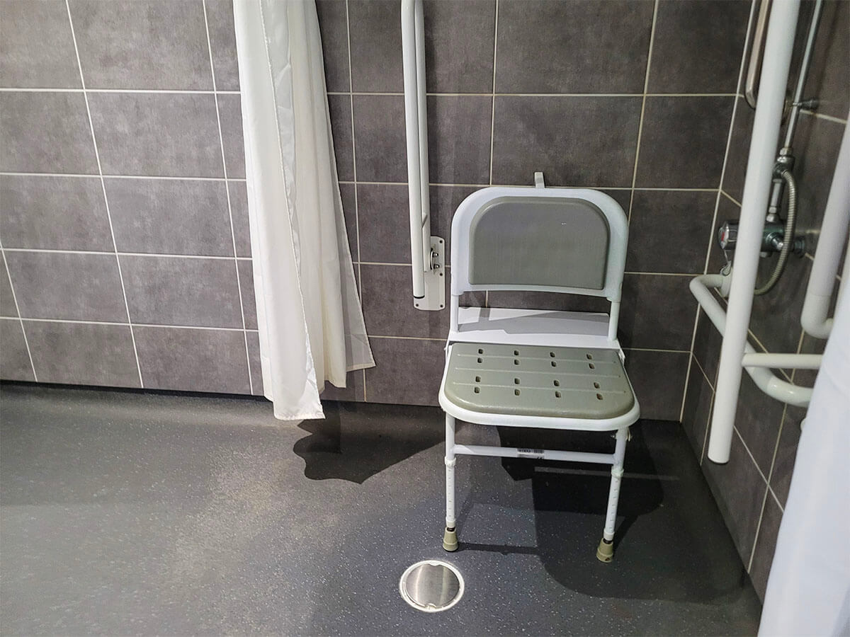 Roll in shower with a white and grey shower seat in a grey tiled wetroom in the wheelchair accessible room at Drimsynie Holiday Village hotel