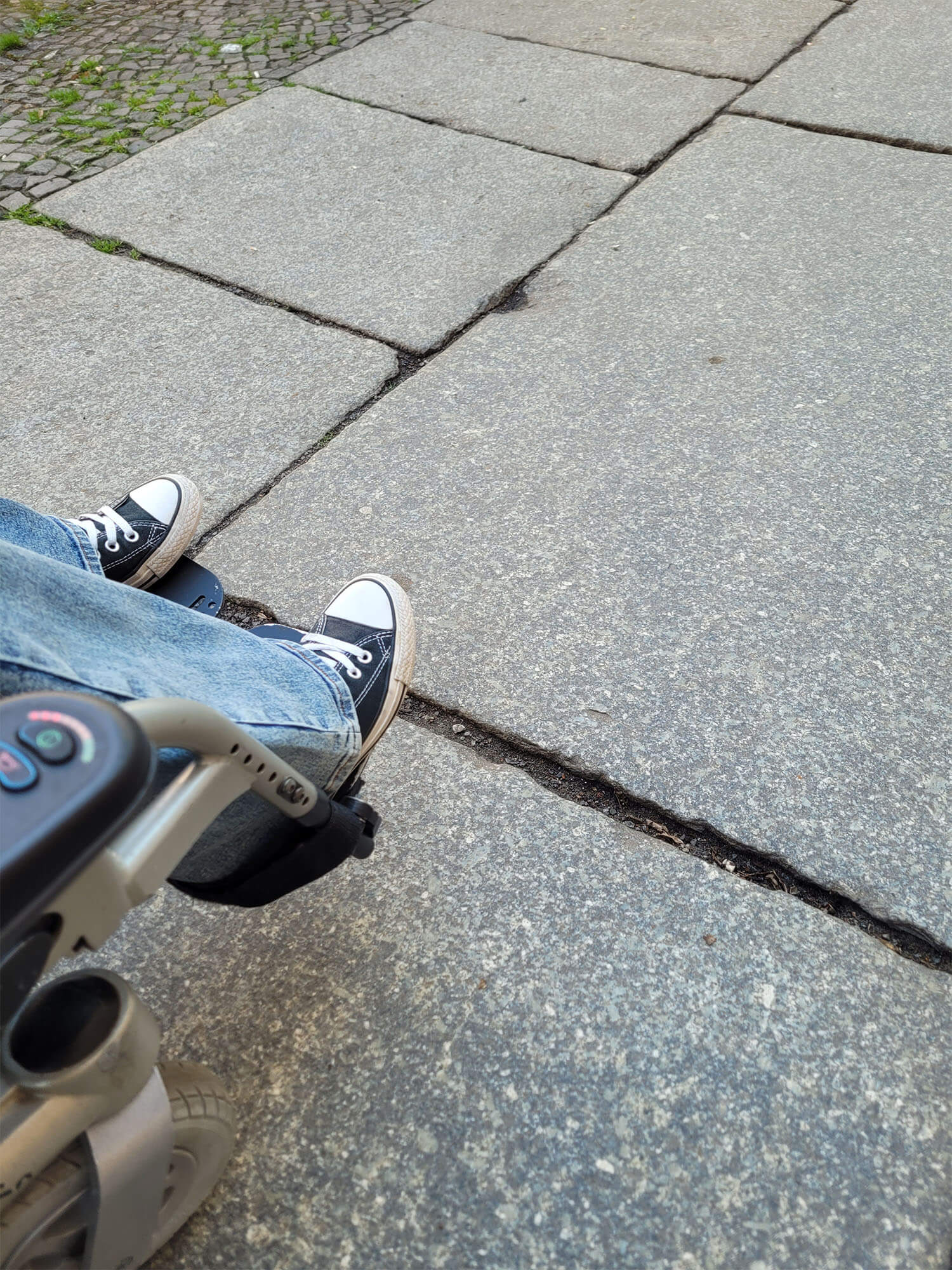 the image shows Emmas legs and feet and part of her wheelchair as she wheels over a cobblestone, uneven and broken path in Berlin