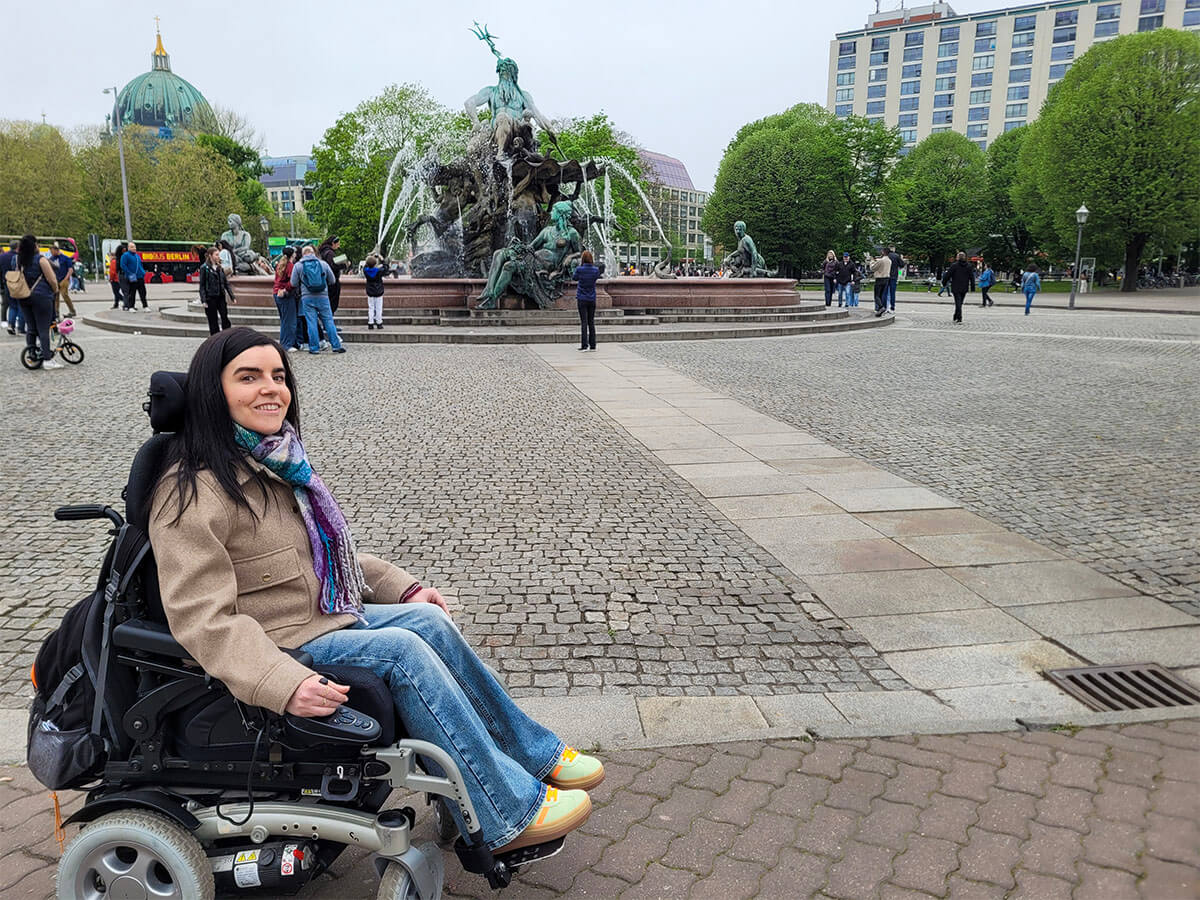 Emma, a powerchair user is sat in front of the Neptunbrunnen (Neptune Fountain)
