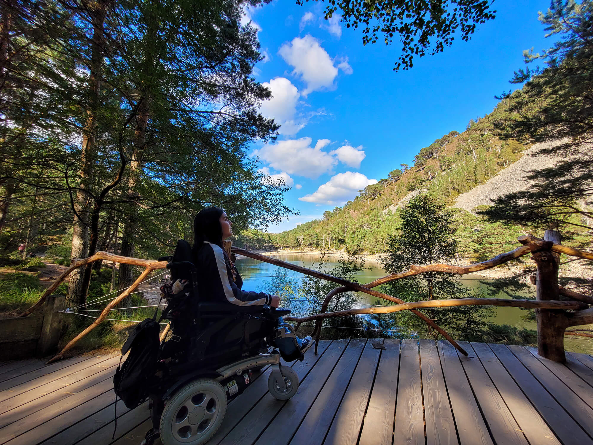Emma sat in her wheelchair on the viewing platform with an Lochan Uaine, the Green Loch in front of her. Emma has her back toward the camera.