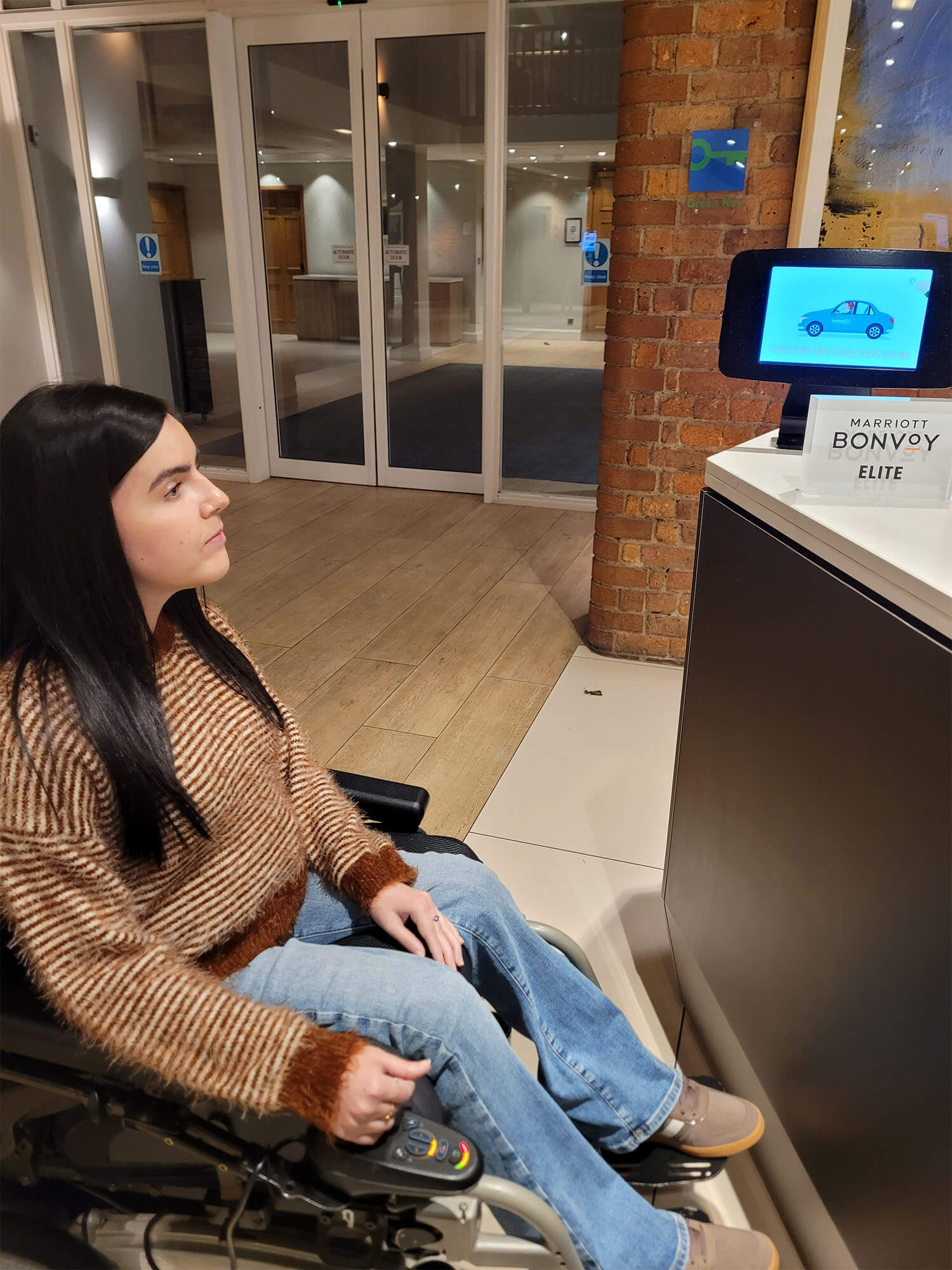 Emma, a wheelchair user, is sat at the check-in desk at the Manchester Marriott Victoria & Albert Hotel