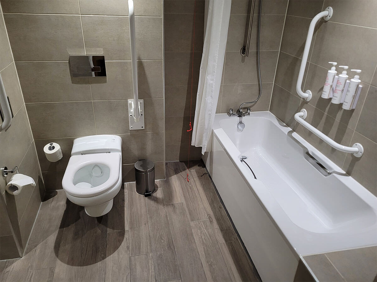 The photo shows the toilet and bathtub in the wheelchair accessible room at Manchester Marriott Victoria & Albert Hotel.